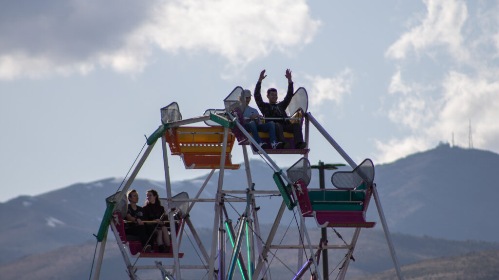 Kids ride the Ferris wheel, putting their hands up smiling at the Biggest Little Festival.