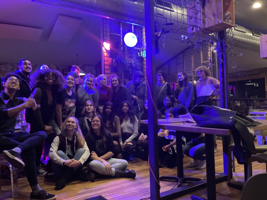 A group photo of 20 people, with some seated on the Laughing Planet's hardwood floor. 