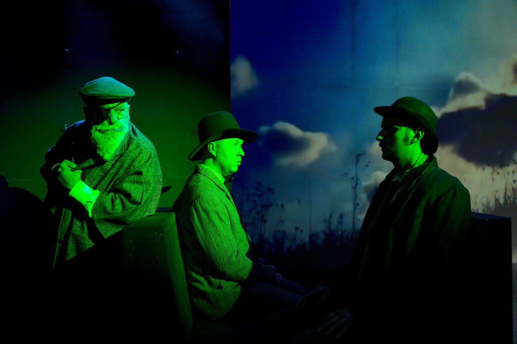 Three actors lit moodily in green against a sky backdrop.