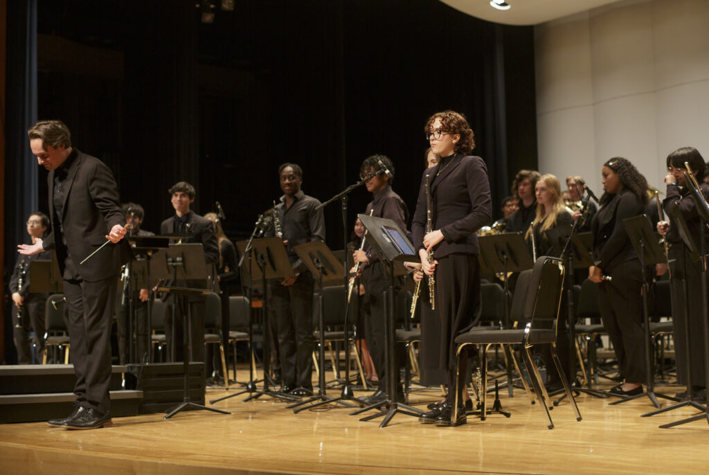 Musicians on stage, surrounding a bowing conductor.