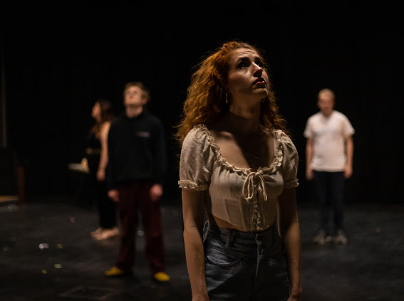 An actress, center, stands staring up. Three other cast members, in various states of blur, surround her.