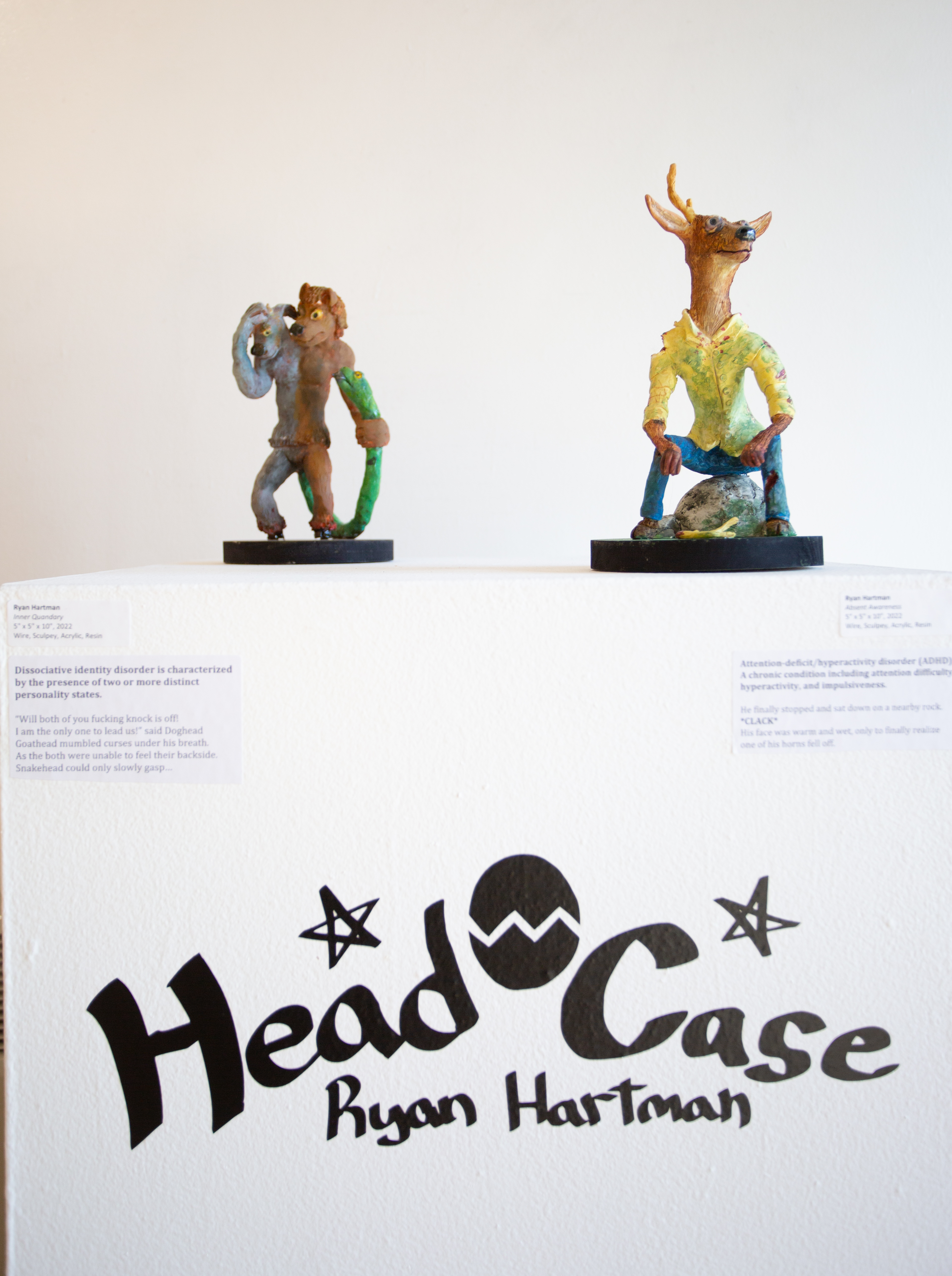 Two clay figures on a podium with the title, "Head Case: Ryan Hartman" at the bottom. The right figure is an anthropomorphized deer in a button-up shirt, with antlers below it on the ground. 