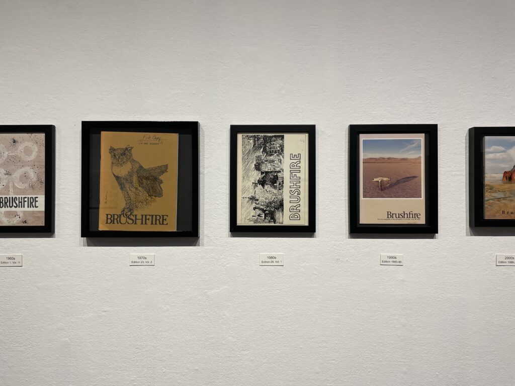 Covers of journals in black frames on a white gallery wall. 