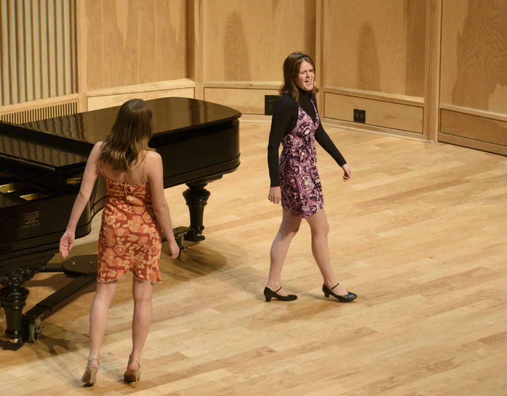 Two singers, one in an orange dress and the other in purple, mid-performance.
