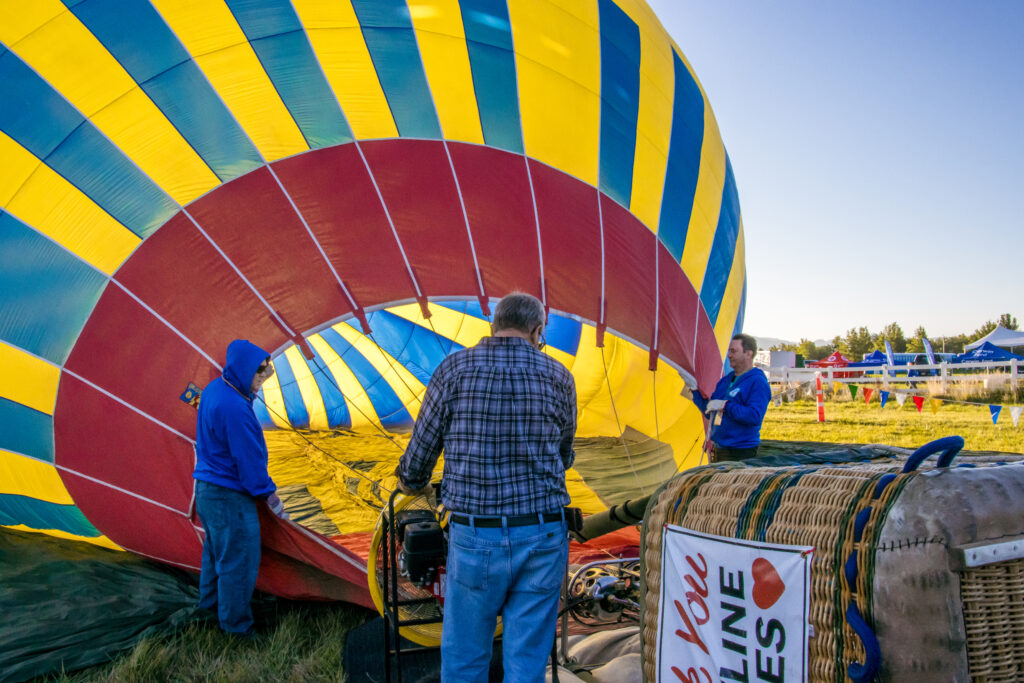 Volunteers stand at the opening of a balloon resting on the ground.