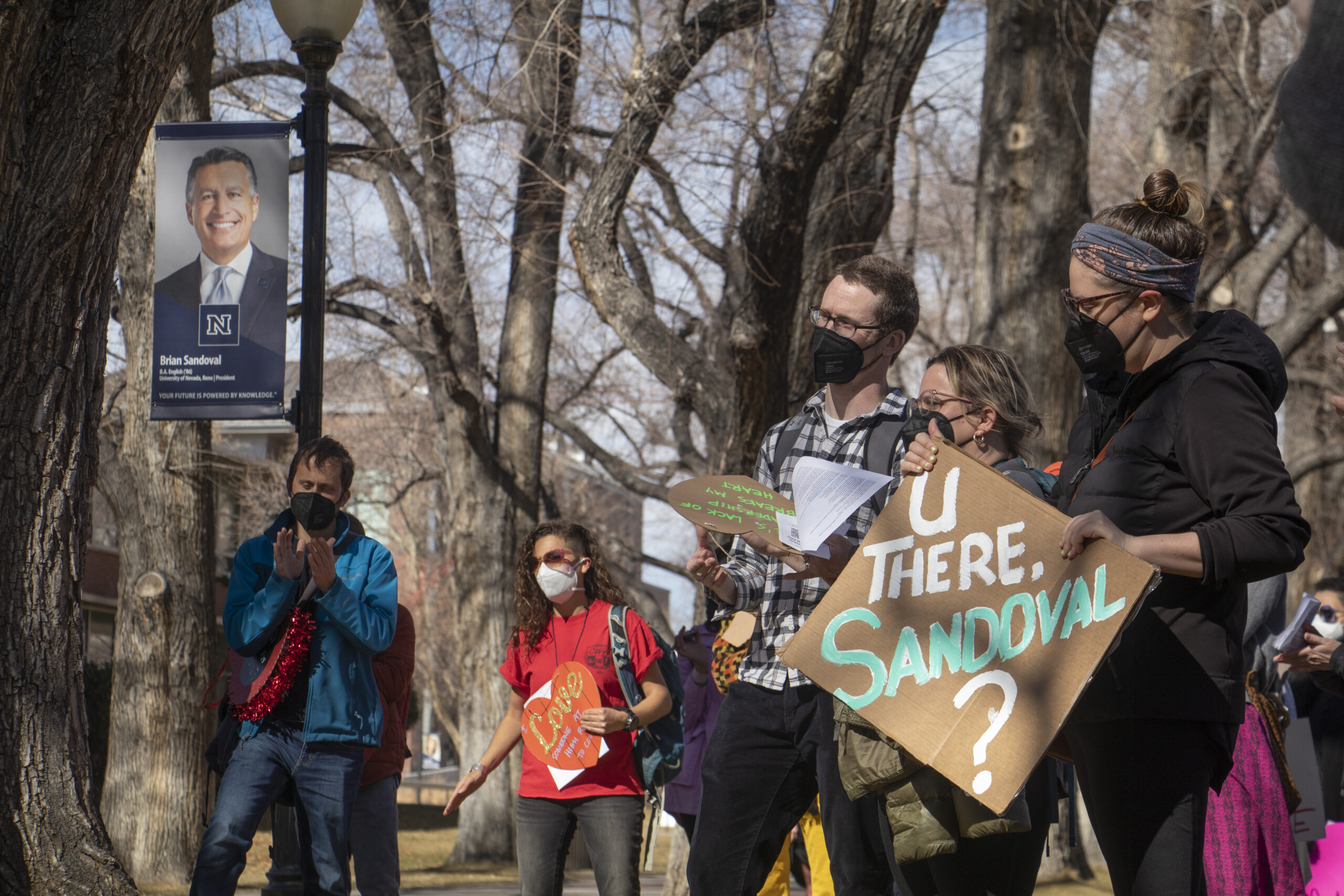 A protester holds a sign calling out Brian Sandoval while standing in front of a poster of him on Feb. 14. Students, faculty and staff at UNR attended a protest organized by Nevada Graduate Student Workers in an attempt to get the mask mandate reinstated.