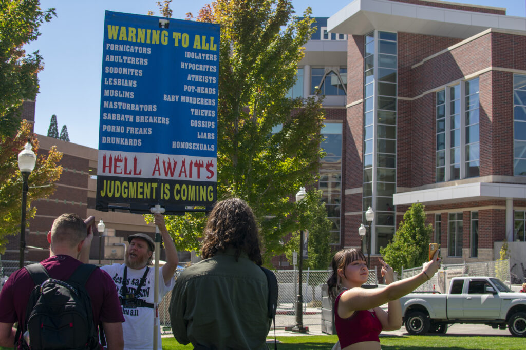 Daniel John Lee holds up a sign that says "Warning to all sinners. Hell awaits. Judgment is coming." in front of students at the E.L Wiegand Fitness Center on UNR campus.