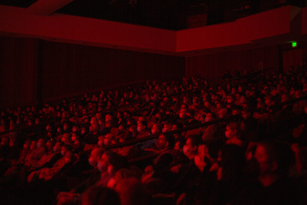 People sit in a theater with red light over them