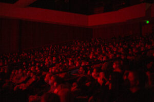 People sit in a theater with red light over them