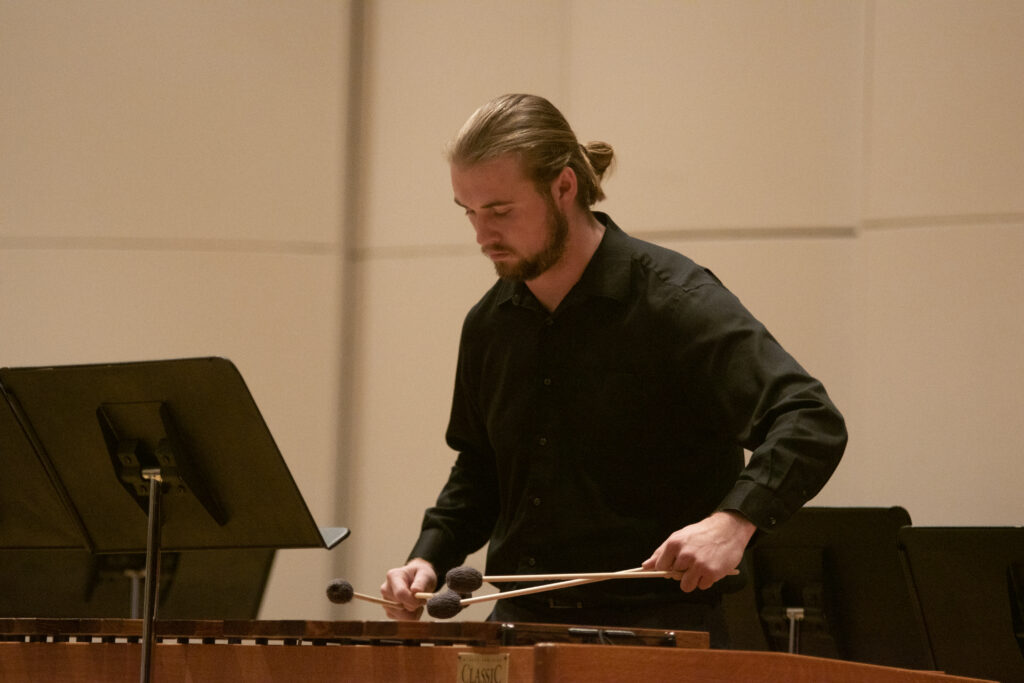 A musician holds fabric mallets in both hands over a xylophone at a concert.