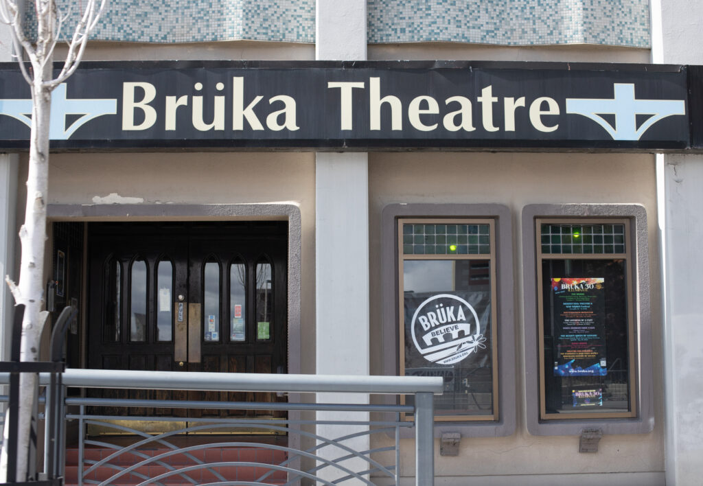 A theatre venue, with "Brüka Theatre" in clear signage over the door. A season poster is visible in the window to the right.