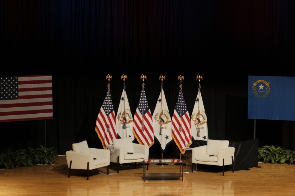 Three white chairs sitting on a stage with flags behind them