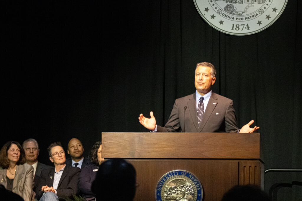 Brian Sandoval stands in front of a podium at the University of Nevada, Reno with the deans of the university sitting behind him as he gives his state of the university speech.