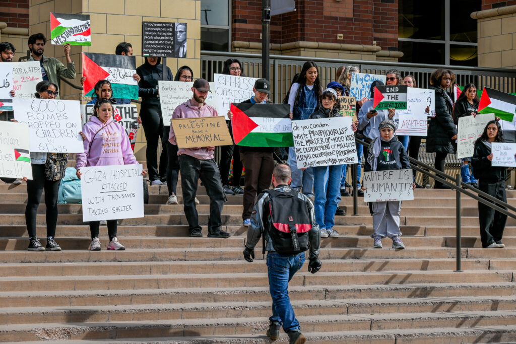 Protestors hold up signs in support of Palestine while a member of the campus community walks up the steps of the library