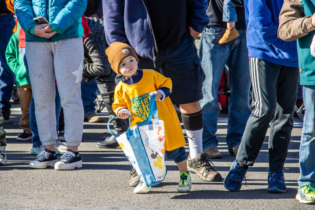 Small kid in yellow leans away from the crowd with an open bag waiting for candy.