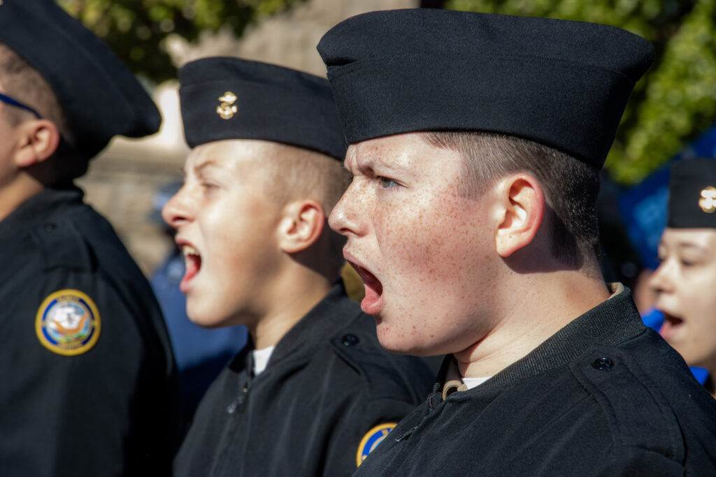 Two people wearing black hats and jackets shout with an open mouth expression.