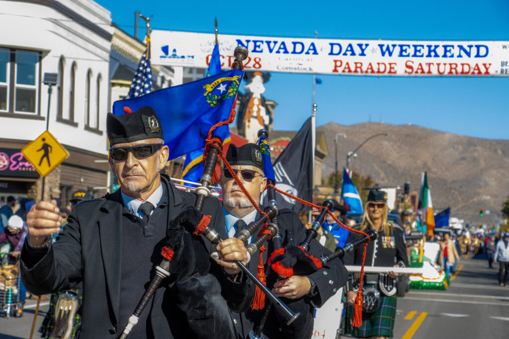 Parade participants march in the street with the Nevada Day Weekend parade banner behind them.