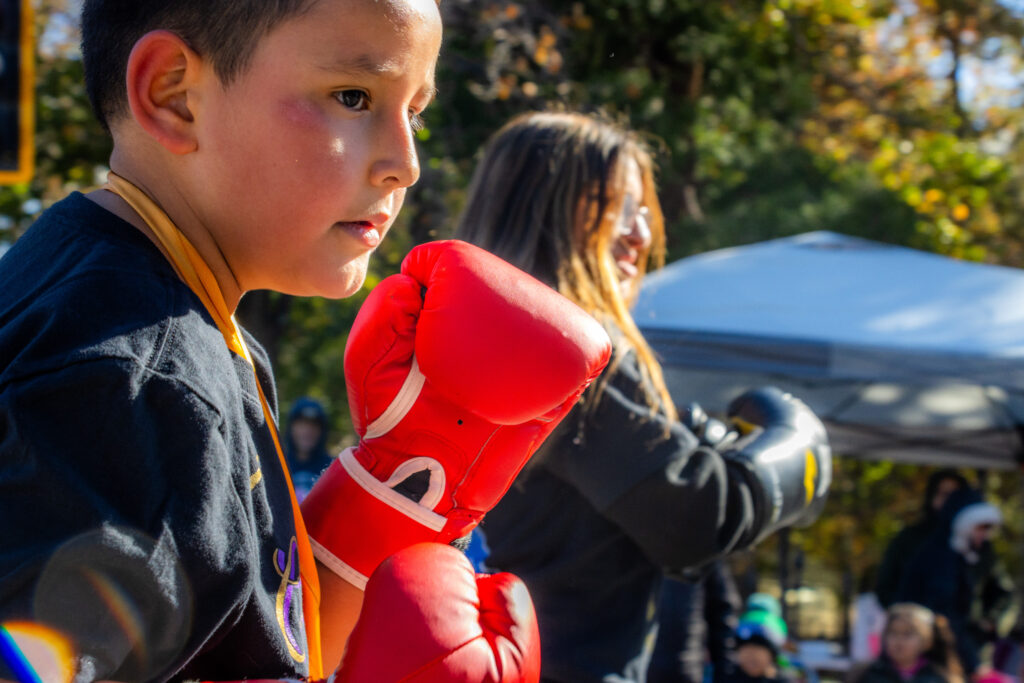 A kid wearing red boxing gloves has a serious expression and a fighting stance.