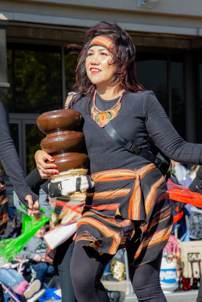 Woman wearing cultural wear smiles, holding a brown item dancing.