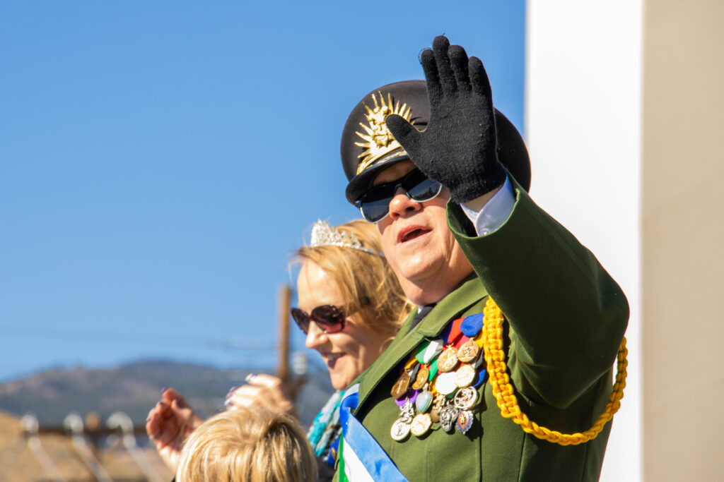 President of the Republic of Molossia, Kevin Baugh, waving with a black glove, hat, and sunglasses. His wife in the background.