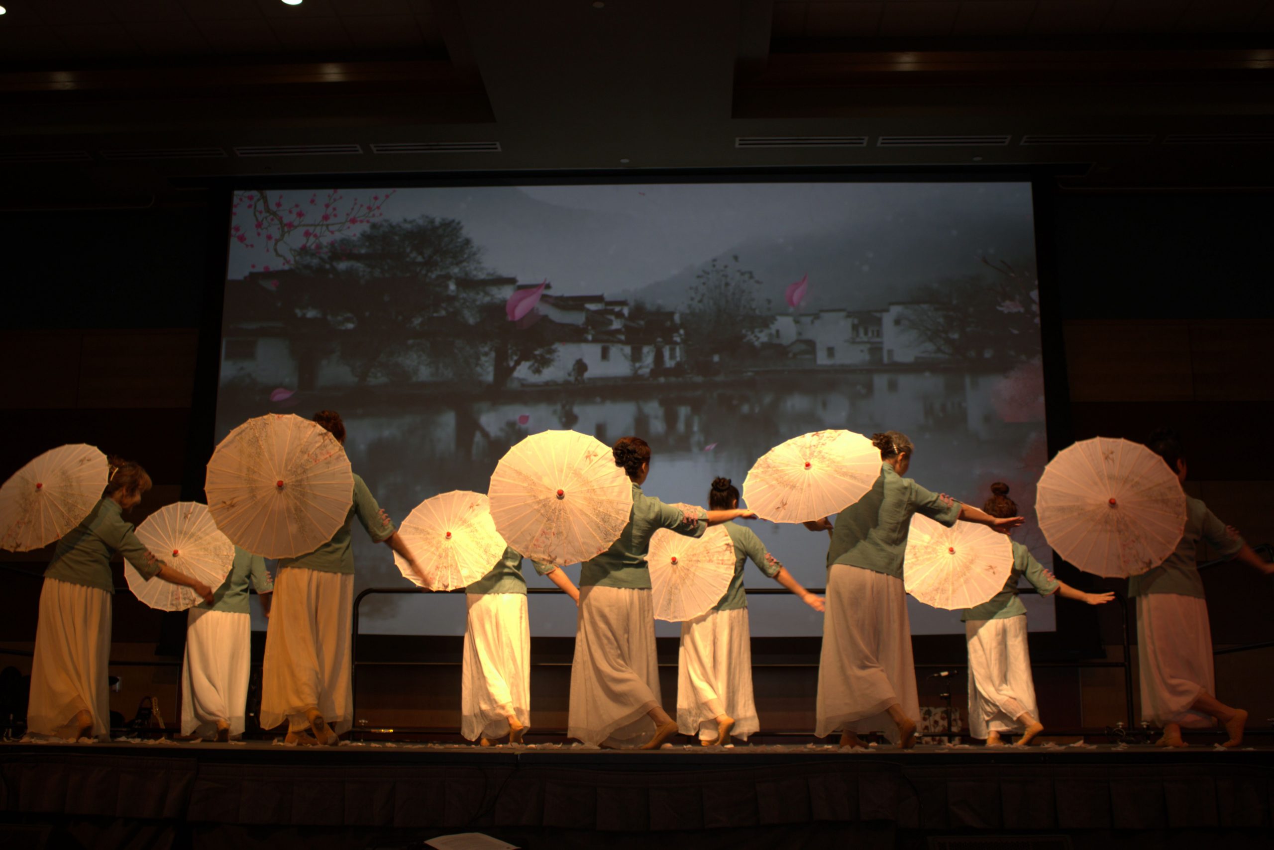 Asian performers with traditional clothing and umbrellas on stage