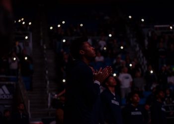Vaugn Weems looks out into the court and the lights are off and the audience holds their phone lights up.