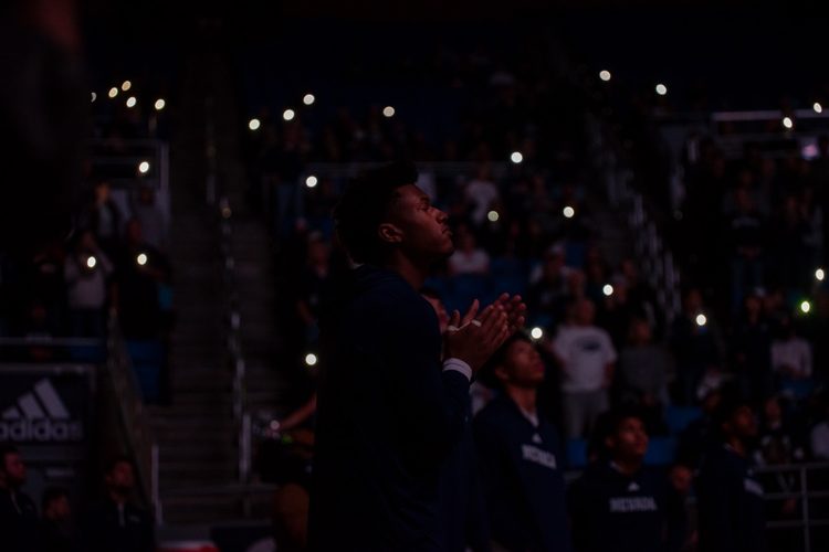 Vaugn Weems looks out into the court and the lights are off and the audience holds their phone lights up.