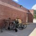 A full bike rack with bikes and scooters. A brick wall is behind the bike rack.