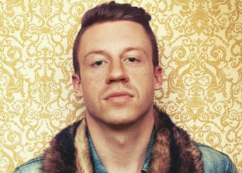 Macklemore stands against a wallpaper background.