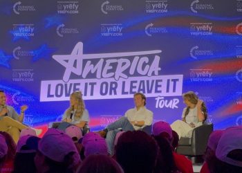 Four seated panelists in front of a large screen that reads, "America, Love It or Leave It."
