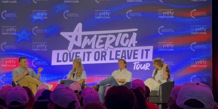Four seated panelists in front of a large screen that reads, "America, Love It or Leave It."