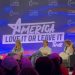 Four seated panelists in front of a large screen that reads, "America, Love It or Leave It."