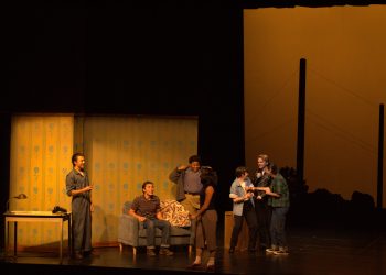 The Outsiders cast conversing on stage during a scene.