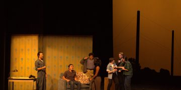 The Outsiders cast conversing on stage during a scene.